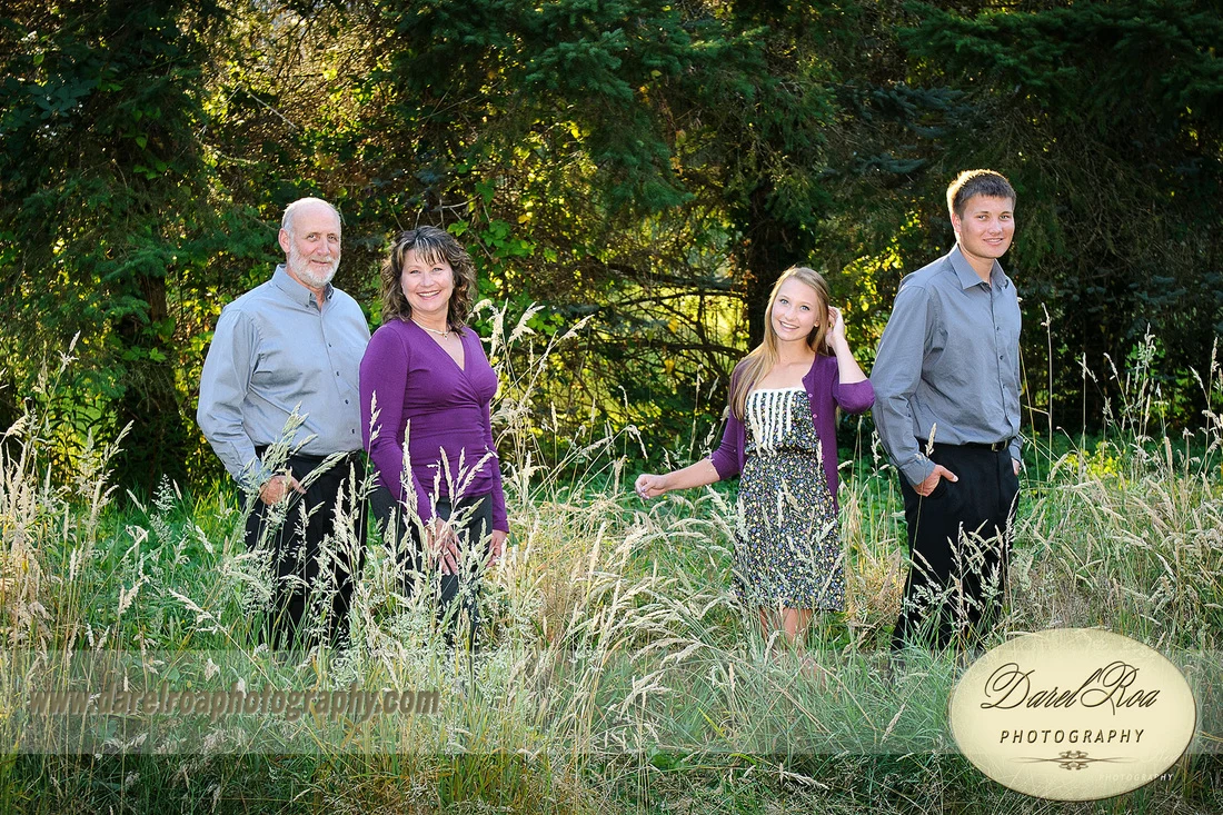 Four people standing in tall grass at the edge of a wooded area.