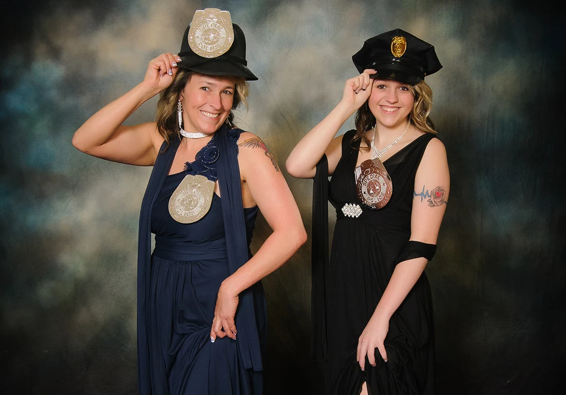 Two smiling women in dresses tipping costume police hats and wearing oversized toy badges.
