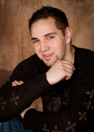 Smiling person in a black shirt resting their chin on one hand against a brown backdrop.
