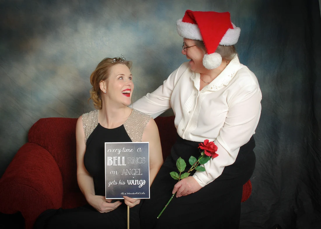 Woman holding a movie-quote sign beside a woman in a Santa hat holding a red rose.