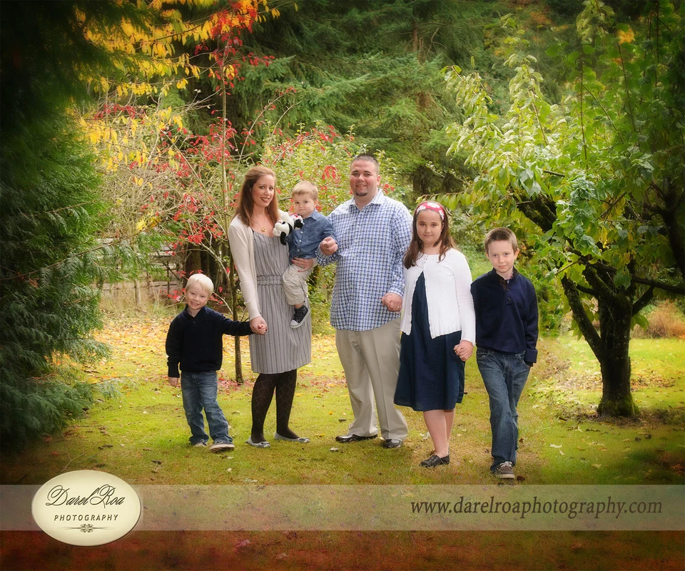 Two adults and four children posing on a lawn beneath trees, with one adult holding a toddler.