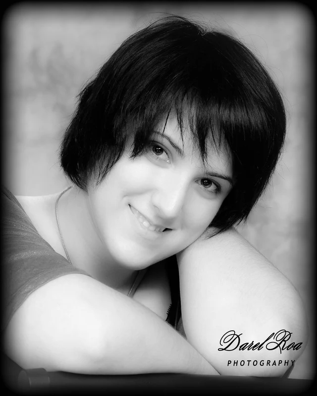 Black-and-white close-up of a smiling person with short dark hair leaning on folded arms.