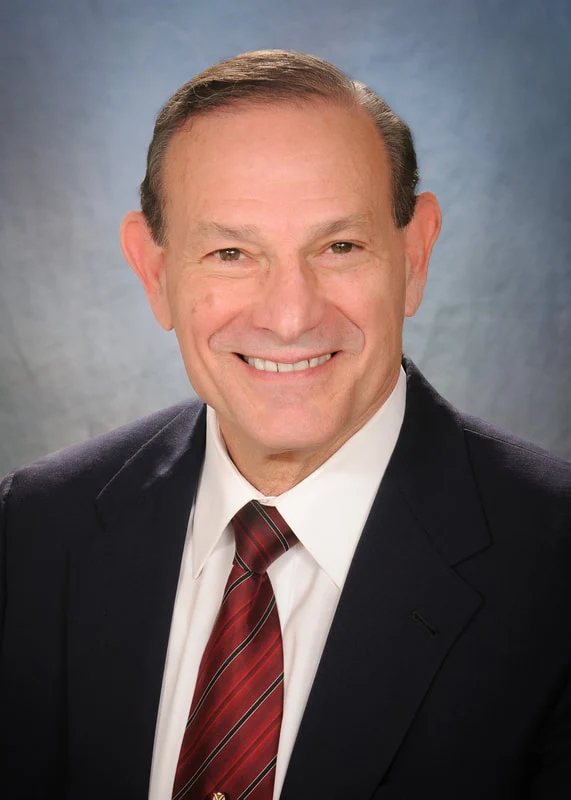 Smiling man in a dark suit, white shirt, and red striped tie against a gray backdrop.