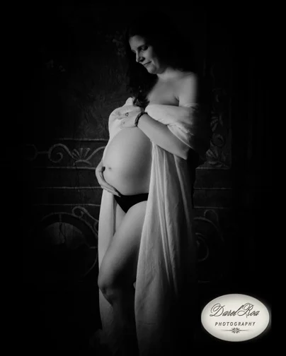 Black-and-white portrait of a woman cradling her bare belly beneath a draped wrap.