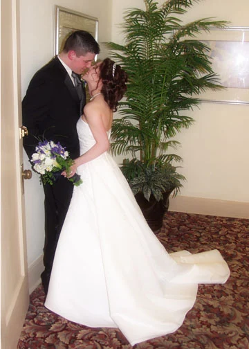 Bride and groom kissing beside a doorway, with her long white gown sweeping across the carpet.
